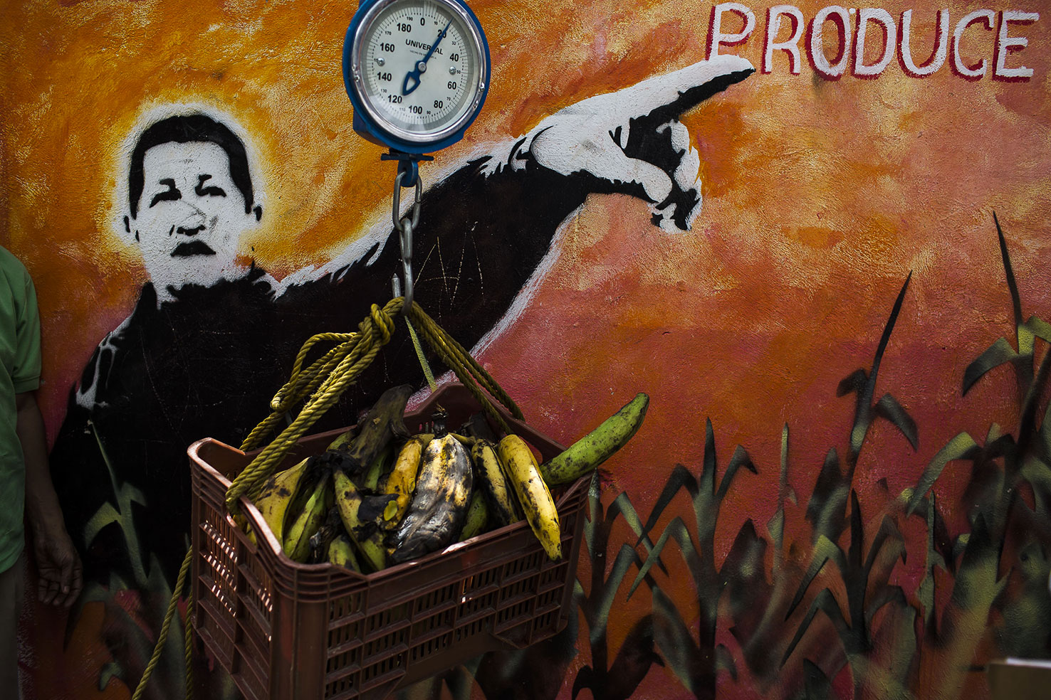 Un operario pesa una caja cargada de verduras junto a un mural del difunto Presidente de Venezuela, Hugo Chávez en el barrio caraqueño de San Agustín. Santi Donaire
