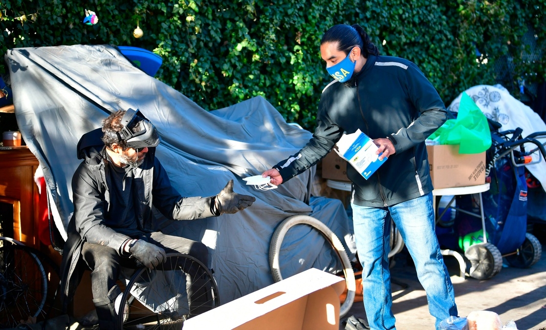Un hombre sin hogar recibe un cubrebocas en Venice, California; en EU hay 66 millones de personas blancas en situación de pobreza. Foto Afp