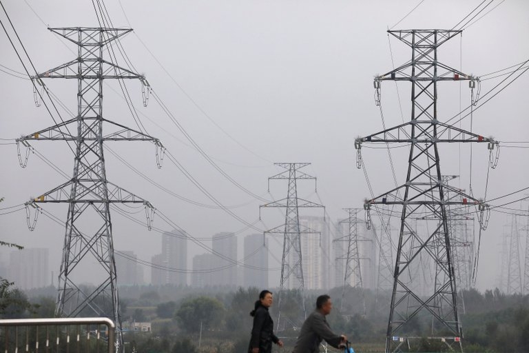 Dos personas pasan por delante de las torres de alta tensión en Shenyang, provincia de Liaoning (Foto: REUTERS/Tingshu Wang)